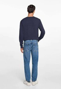 Mornarsko modra majica z dolgimi rokavi in okroglo ovratnikom, v kombinaciji s svetlomodrimi kavbojkami z zadnjimi žepi in zoženimi hlačnicami. Bele superge.