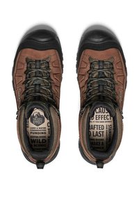 Een paar bruine en zwarte wandelschoenen met patroonveters, gevoerde kraag en bedrukte binnenzolen met teksten over natuurbehoud en buitenactiviteiten.
