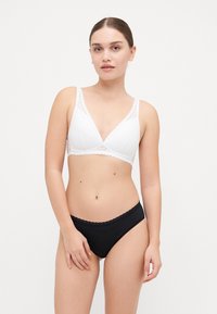 Hvit bralette med blonder, i trekantet form, supplert med svarte undertøy med bølget midje. Glatt tekstur, sømløst design.