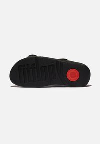 Suela de goma negra con patrones texturizados, que presenta un acento circular rojo y la marca "fitflop" en relieve. Diseño plano y ancho para mayor estabilidad.