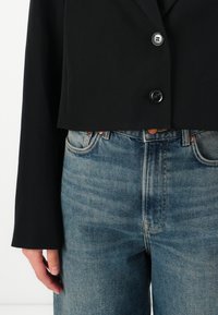 Svart kort blazer med knappstängning och långa ärmar, tillsammans med ljusblå högmidjade jeans med blekta detaljer och kopparnitar.