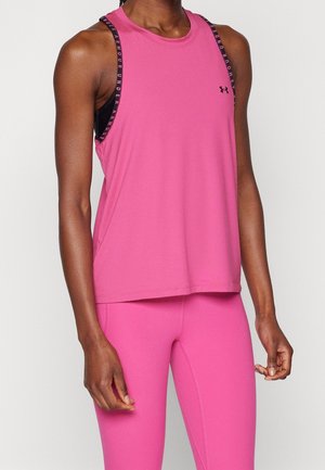 Persona vistiendo una camiseta deportiva sin mangas de color rosa brillante y leggings, con un sujetador deportivo negro visible bajo las tiras de la camiseta sin mangas con la marca "Under Armour".