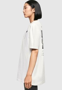 Witte katoenen t-shirt met korte mouwen, losse pasvorm, met een zwart grafisch ontwerp op de achterkant en subtiele tekstdetails op de voorkant.