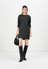 Mørkegrå langermet kjole med rett snitt, kombinert med knelang, svarte støvler og en liten svart veske med en skrukket håndtak.