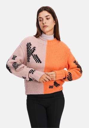 Strickpullover in Pink und Orange mit geometrischen schwarzen Mustern an den Ärmeln. Breite, gerippte Bündchen und runder Ausschnitt. Grobe Textur.