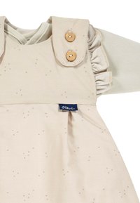 Beiges Kleid mit rüschigen Schultern, Holzknöpfen und dezentem Sternenmuster. Verfügt über ein Logoband und einen weichen, strukturierten Stoff.