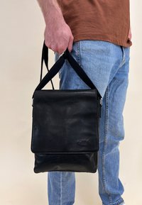 Borsa a tracolla nera in pelle con pattina, caratterizzata da una superficie testurizzata e una tracolla removibile. Design semplice, dettagli minimal.