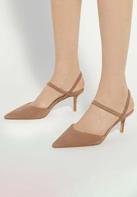 Chaussures à talons hauts en daim brun clair, avec un bout pointu, un dos ouvert et une bande de cheville. Présentent un talon mince de 5 cm et une texture lisse.