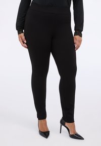 Černé elastické legíny s vysokým pasem, s rozparky na kotnících. V kombinaci s černými lodičkami s špičatou špičkou a topem s dlouhým rukávem.