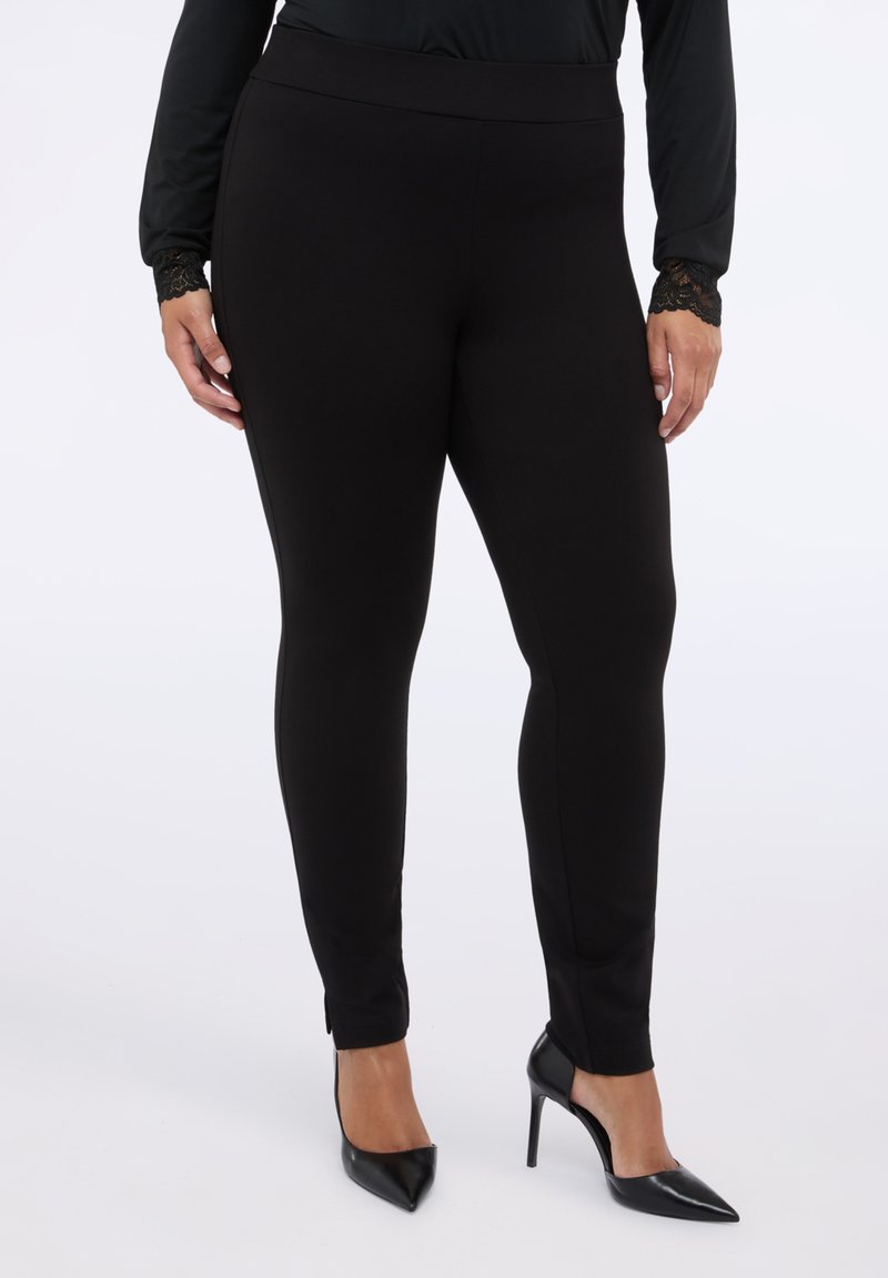 Černé elastické legíny s vysokým pasem, s rozparky na kotnících. V kombinaci s černými lodičkami s špičatou špičkou a topem s dlouhým rukávem.