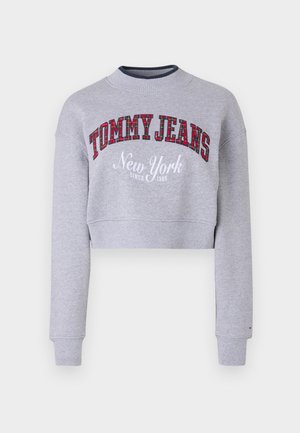Harmaa lyhythihainen collegepaita, jossa on ribbireunus kauluksessa ja hihoissa. Edessä on "TOMMY JEANS" punaisessa tartaankuviossa ja "New York" valkoisena brodeerauksena. Pehmeä kangas.