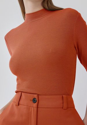 Ribbet orange top med høj hals og trekvart lange ærmer, kombineret med matchende højtaljede bukser med sort knappedetalje.