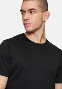 Camiseta negra de manga corta hecha de tejido texturizado, con cuello redondo y costuras mínimas, diseñada para un ajuste ceñido.