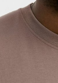 Kortærmet T-shirt i afdæmpet brun stof med en glat tekstur. Har en rund halsudskæring og subtile syninger.