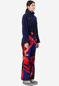 Pantaloni da sci con un motivo astratto vivace in rosso, blu e nero. Presentano bretelle nere regolabili e un logo Kappa sul lato.