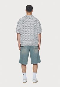 Korte mouwen zwart-wit patroon shirt met een losse pasvorm, gecombineerd met lichtblauwe denim shorts en witte sokken met merklogo.