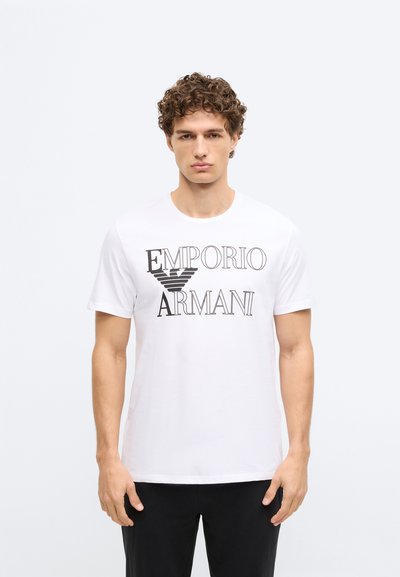 Balta kokvilnas T-krekls ar īsām piedurknēm un melnu uzdrukātu tekstu “EMPORIO ARMANI.” Vienkāršs apaļš kakla izgriezums, gluda tekstūra un parasta piegriezuma.