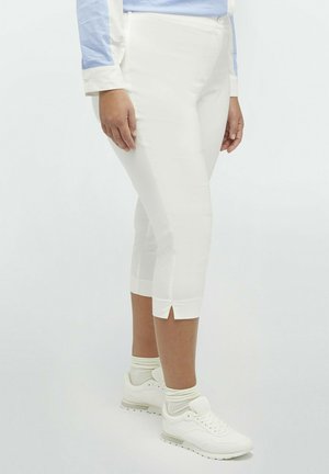 Pantalones recortados blancos con aberturas laterales, hechos de una tela suave. Combinados con zapatillas blancas, de perfil bajo y cordones.