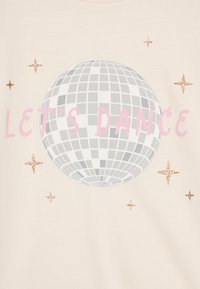 Camicia beige chiara con una grande grafica di una palla da discoteca grigia, testo rosa "LET'S DANCE" e accenti di stelle glitter dorate.