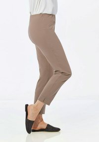 Pantalons marron, extensibles, de longueur cheville avec une texture lisse, une taille élastique et une poche zippée sur le côté. Associés à des chaussures noires à enfiler en tissu tissé.