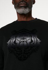 Sudadera negra con un destacado gráfico de tigre texturizado en tonos de gris, con intrincados detalles en línea en la cara y el pelaje.
