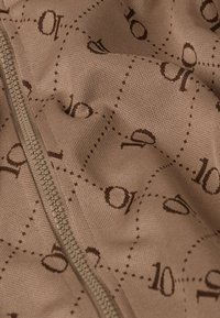 Tela marrón con un patrón de cuadrícula que incluye el número '10' y detalles circulares. Un cierre de cremallera corre a lo largo de un lado. Textura suave.