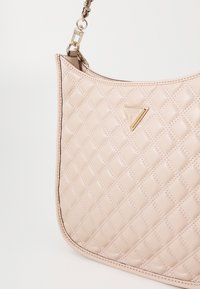 Quilted beige håndtaske med en glat læderstruktur, trekantet logoaccent og guldbeslag. Har en skulderrem og sort syning.