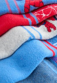 Toallas apiladas en tonos de rojo, azul y gris, con patrones a rayas y motivos de langosta, hechas de un tejido suave y texturizado.