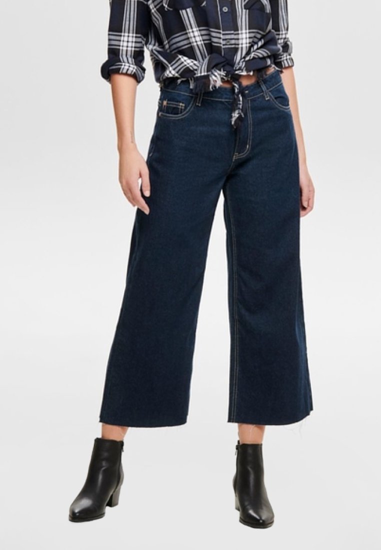 Mörkblå vida jeans med hög midja, tillverkade av denim. Har kontraststickningar och en avslappnad passform. Matchas med svarta ankelstövlar.