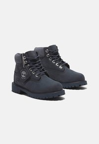 Botas de tobillo impermeables de ante en color azul marino, con ojales de metal, cuello acolchado y suela de goma resistente con un patrón de textura en el tread.