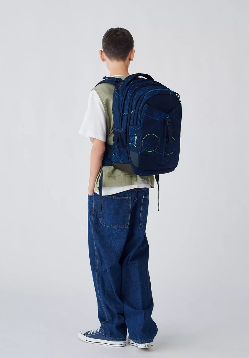 Marineblaue Rucksack mit geometrischen Mustern und grünen Akzenten, ausgestattet mit mehreren Fächern und gepolsterten Trägern, getragen von einem Kind.