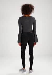 Top gris de manga acampanada combinado con jeans ajustados negros y zapatillas grises. El top tiene un escote redondo y los jeans cuentan con bolsillos traseros.