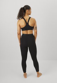 Fekete sportos melltartó vastag pántokkal és logós pánttal, magas derekú fekete leggings-szel párosítva. Sima textúra, testhez simuló dizájn.