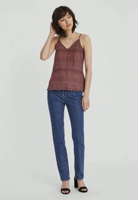 Weinrotes Spitzentop mit V-Ausschnitt, das einen gewellten Saum und filigrane Muster aufweist, kombiniert mit dunkelblauen Slim-Jeans.