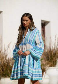 Vestido azul y blanco con estampado, de manga larga, escote en pico y forma fluida. Presenta diseños geométricos y una tela texturizada.