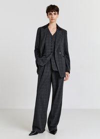 Completo grigio a quadretti con giacca doppiopetto, gilet abbinato e pantaloni larghi. Presenta un colletto nero e dettagli con bottoni.