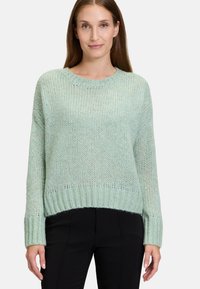 Ljust grön stickad tröja med rund hals, ribbade ärmslut och nederkant, med en lös passform och texturerad tyg. Bärs med svarta byxor.