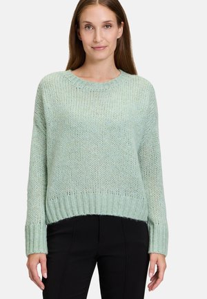 Pull en tricot vert clair avec un col rond, des poignets et un ourlet côtelés, doté d'une coupe ample et d'un tissu texturé. Porté avec un pantalon noir.