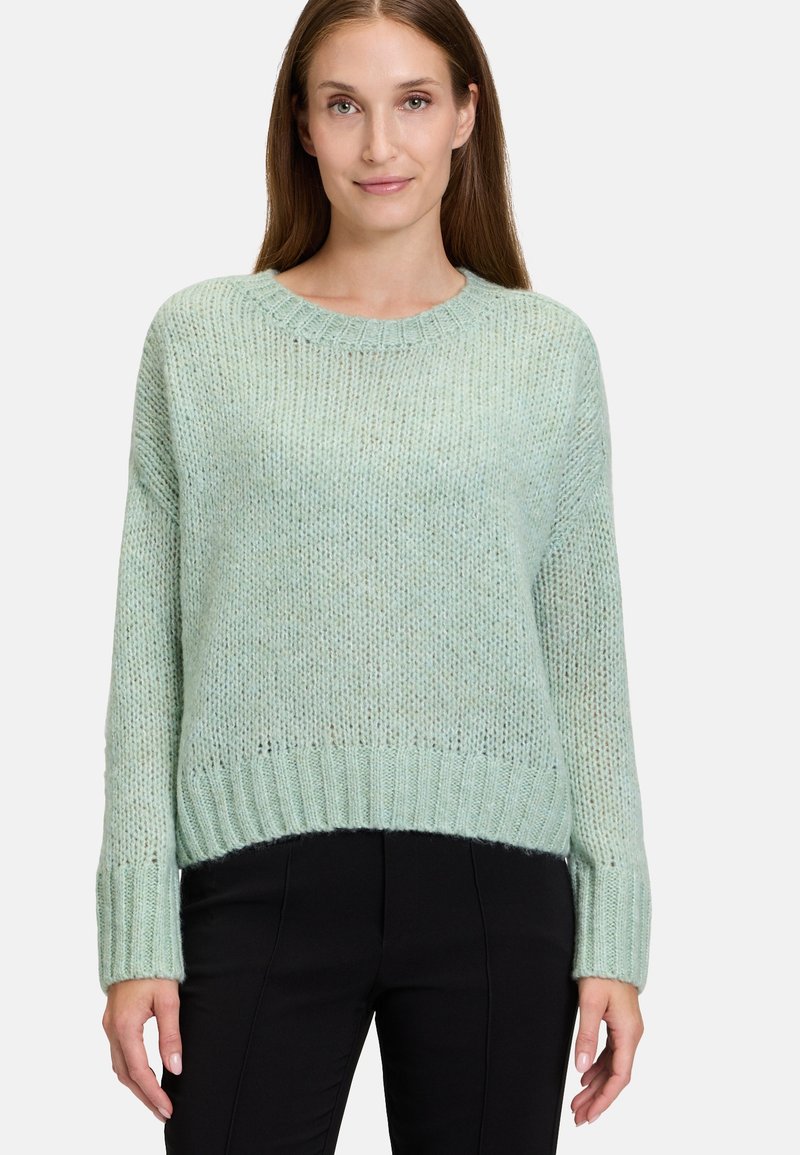 Ljust grön stickad tröja med rund hals, ribbade ärmslut och nederkant, med en lös passform och texturerad tyg. Bärs med svarta byxor.