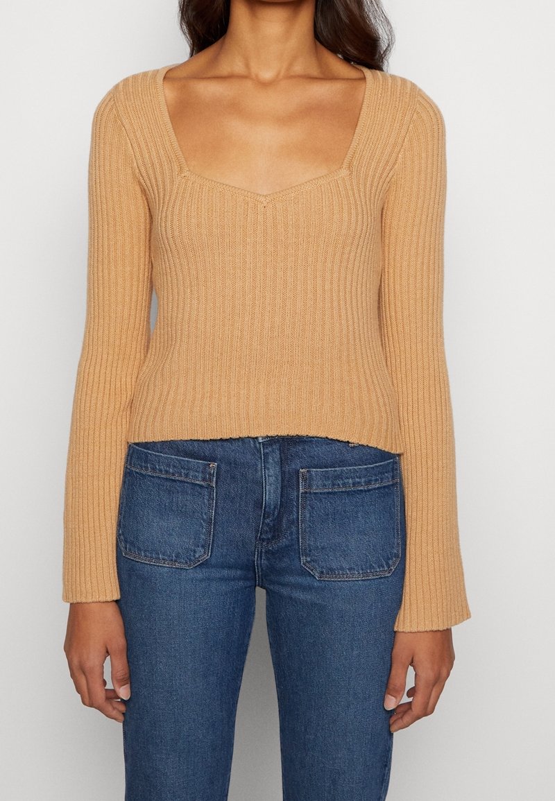 Beige ribbad stickad tröja med fyrkantig halsringning och långa ärmar, med en kortad nederkant och texturerad finish. Bärs med blå jeans.