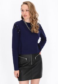 Maglione corto blu navy con lavorazione a maglia testurizzata e dettagli in pizzo nero sui lati delle spalle, abbinato a una minigonna in pelle nera con tasche con zip.