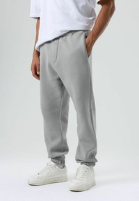 Lichtgrijze sweatpants met een elastische tailleband en boorden, voorzien van zijzakken en een zachte textuur, gecombineerd met witte sneakers.