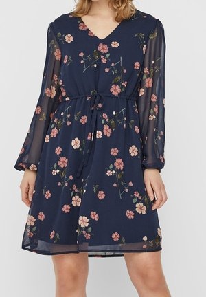 Laivastonsininen kukkamekko, jossa vaaleanpunaisia kukkia, läpikuultavat pitkät hihat, V-aukko ja vyötärön solmimisnauha, polvipituinen.