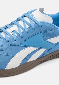 Lichtblauwe sportschoen van suede en leer. Heeft witte accenten, een platte rubberen zool en ronde veters.