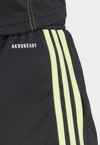 Shorts sportivi neri con tre strisce verticali verde lime e logo "AEROREADY", realizzati in un tessuto liscio e strutturato.