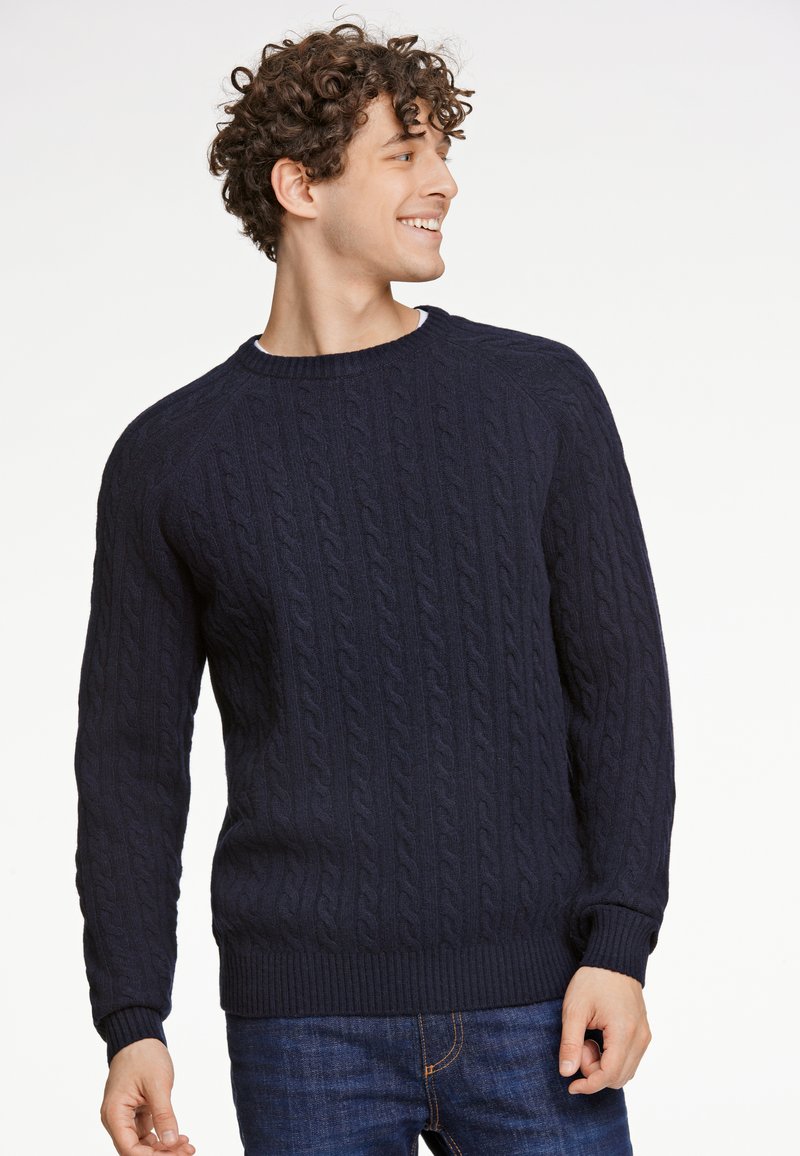 Marineblauer Kabelstrickpullover mit Rundhalsausschnitt, gerippten Säumen und Bündchen. Über einer blauen Jeans getragen, nutzt er ein strukturiertes Muster und eine taillierte Passform.