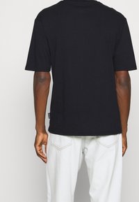 Černé tričko s krátkým rukávem, rovného střihu, vyrobené z bavlny. Na levé straně lemu se nachází malá label značky.