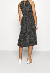 Svart ärmlös klänning med vita prickar, lager-på-lager kjol och nyckelhålsdetalj på ryggen. Matchad med vita sandaler med blockklack.