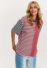 Oversized koszulka w paski z czarnymi, różowymi i pomarańczowymi sekcjami, z haftowanym motylem na klatce piersiowej. Materiał z mieszanki bawełny.