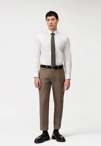 Camicia bianca a maniche lunghe, cravatta verde scuro, pantaloni marroni su misura e scarpe nere. Design elegante con tessuto liscio e vestibilità classica.